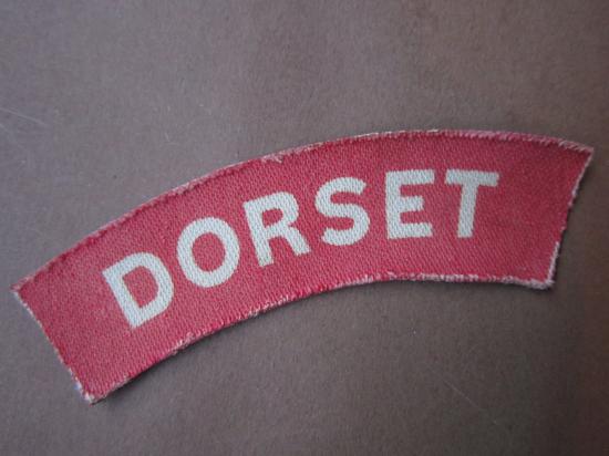 A nice un-issued printed white on red Dorset Regiment shoulder title
